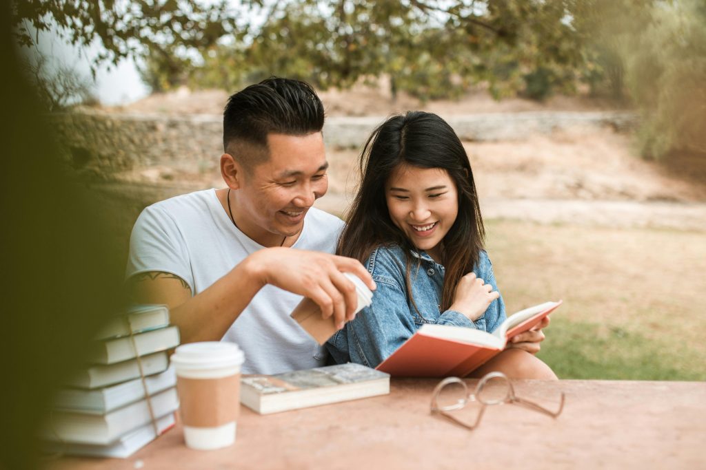 A couple sits outdoors, sharing a book and laughing together, using bonding as a technique for managing and dealing with triggers.