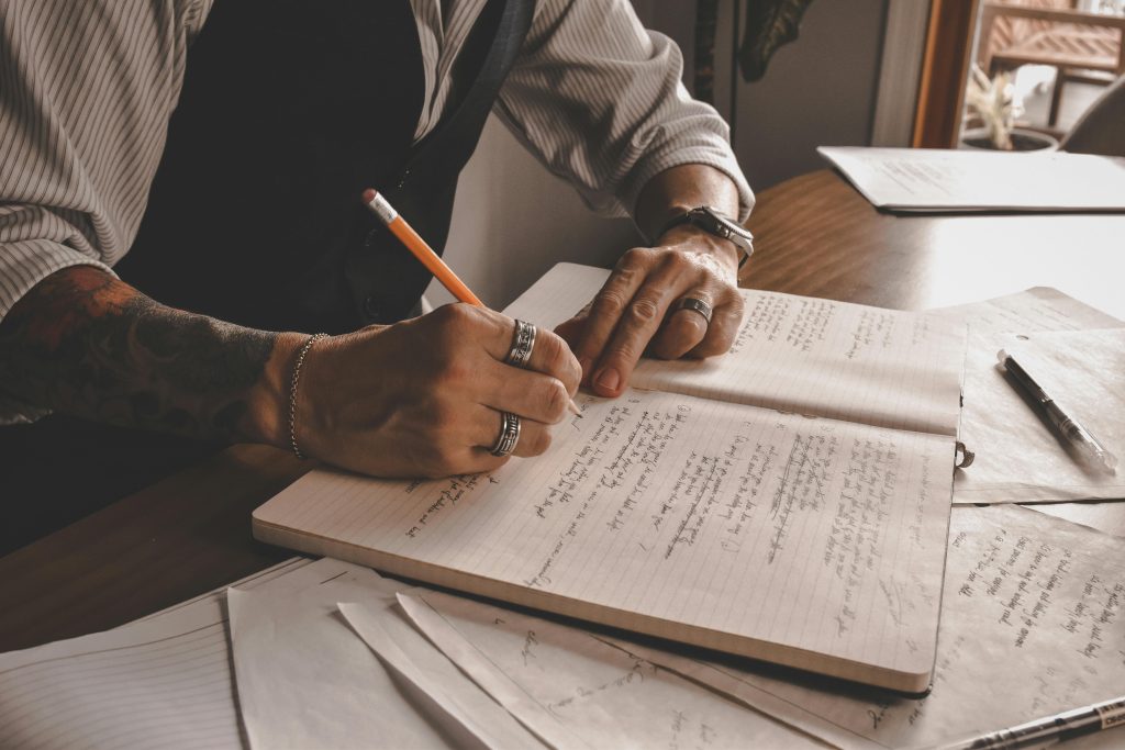 Man with tattoos deeply focused on writing in a journal, a therapeutic method to overcome ptsd triggers.