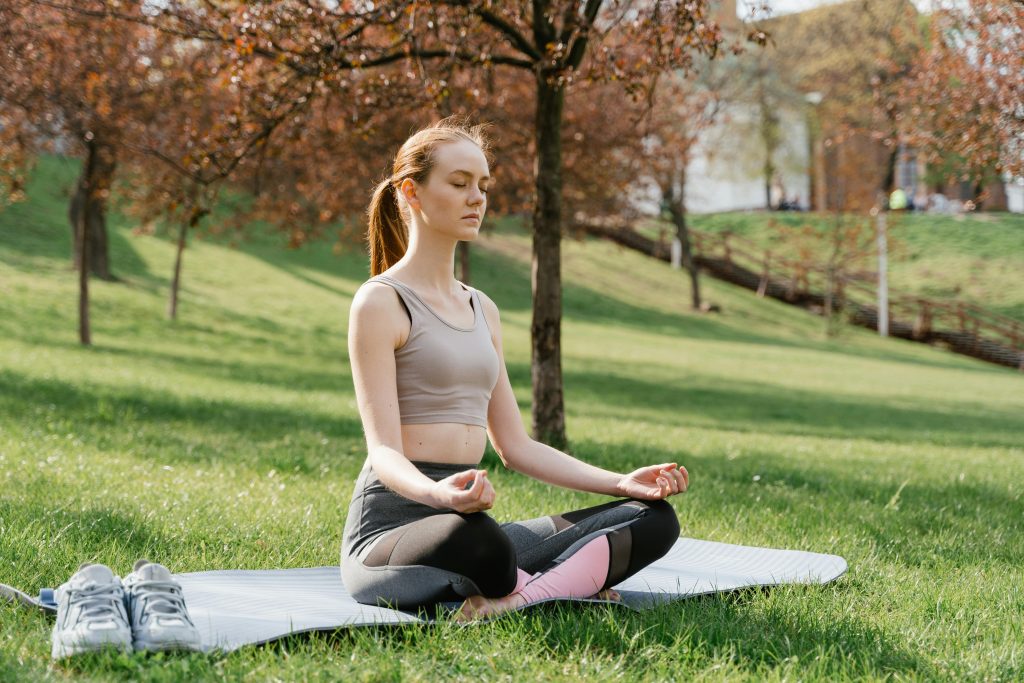 Woman meditating in a park, practicing self-care strategies.