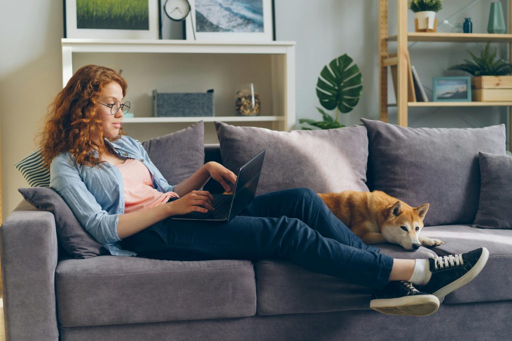 A woman with a laptop and her dog on the sofa, researching types of therapists for the right match.