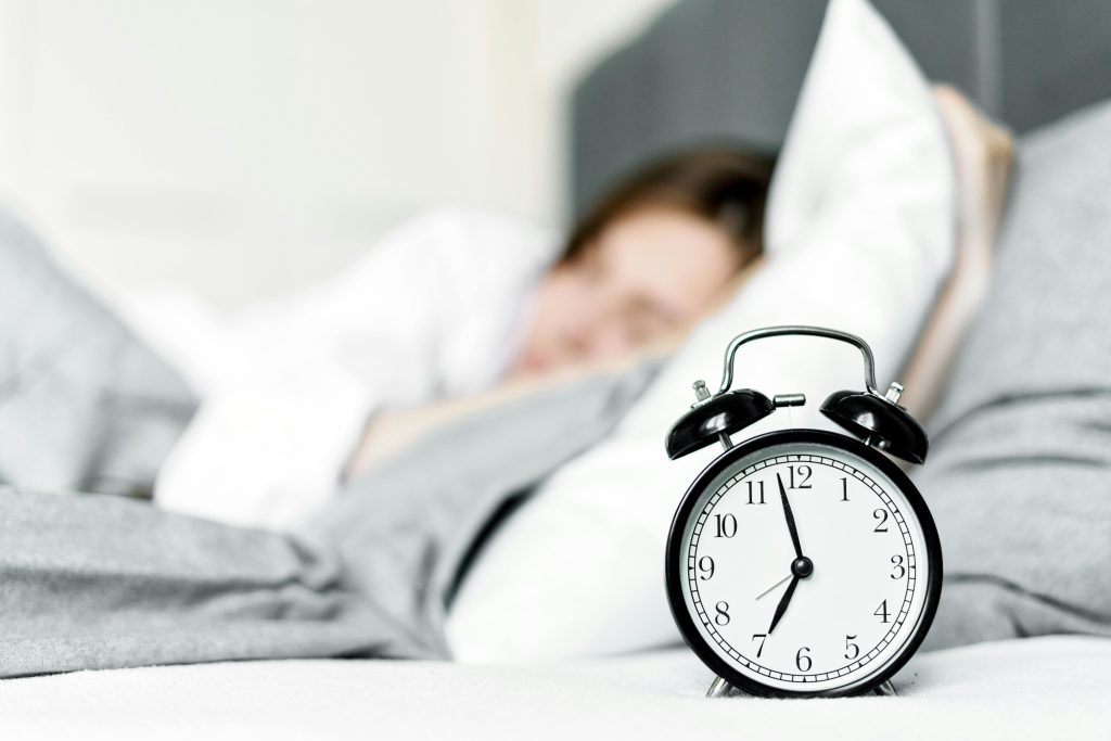 Woman asleep with a visible alarm clock highlighting the importance of sleep for mental health.