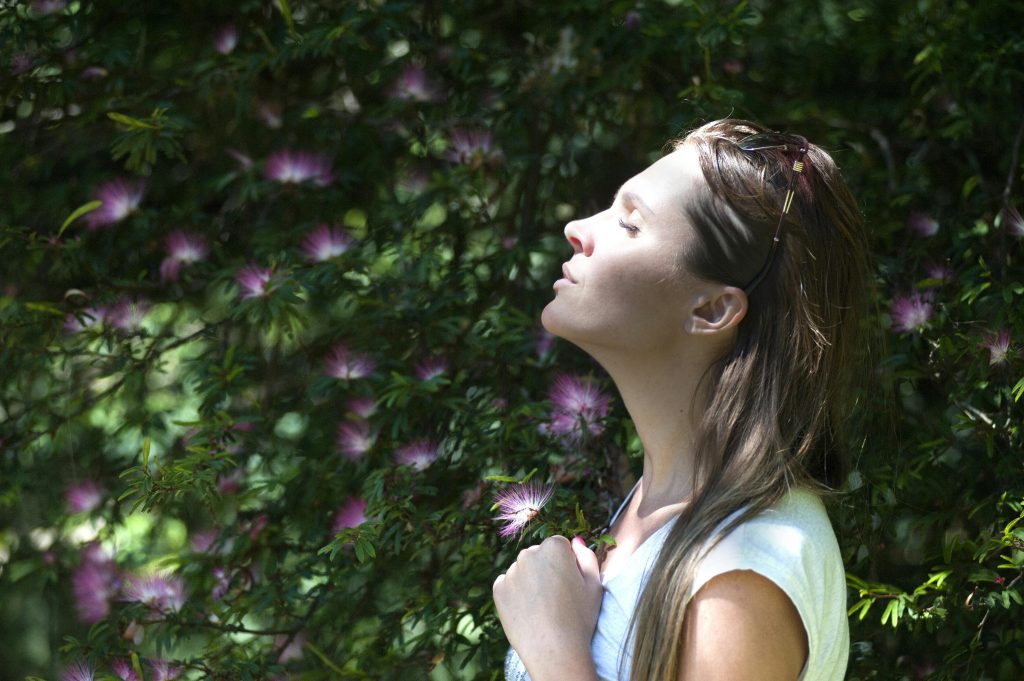 Woman in a serene pose, eyes closed, feeling the peaceful ambiance of a lush garden, illustrating the connection between mind and nature.