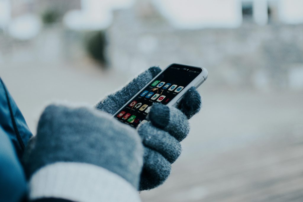 Person in winter gloves using a smartphone, experiencing halloween fomo.