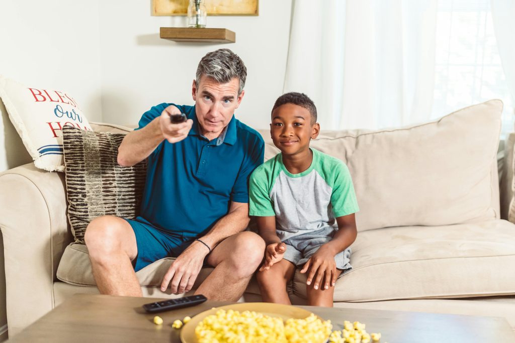 Father and son watching tv together, displaying a moment of children contentment.