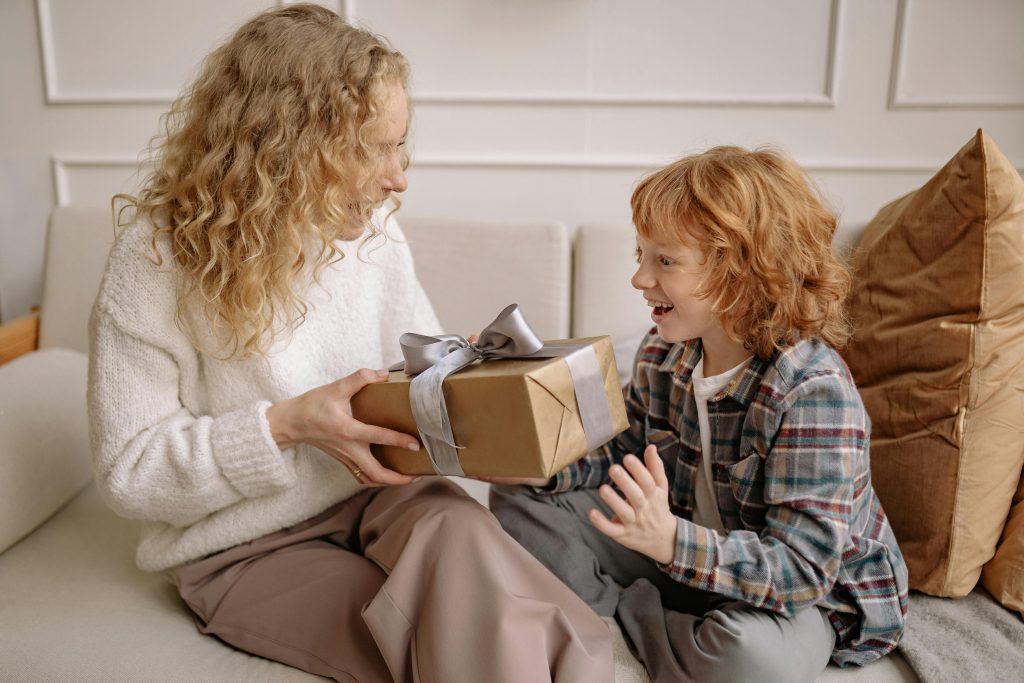 A joyful moment of children contentment as a mother gifts her child a present, showcasing a warm, loving interaction indoors.