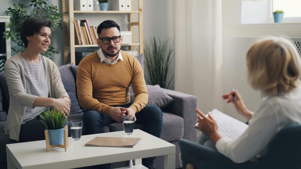 A couple sits with a therapist during a couples therapy session, discussing their relationship dynamics in a supportive environment.