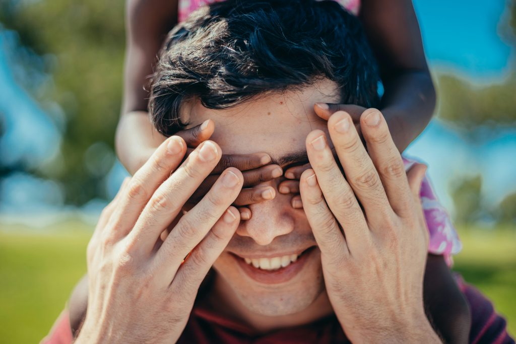 A child playfully covers an adult's eyes in a park, symbolizing the lasting impact of childhood trauma on adult relationships.