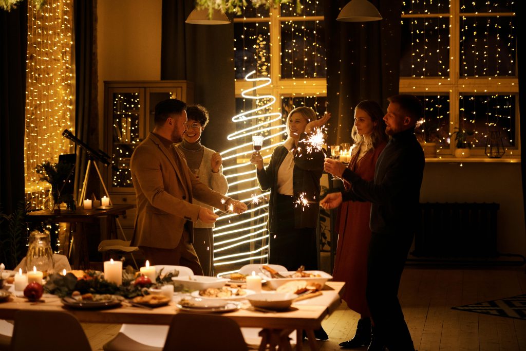 A group of friends enjoying sparklers during a festive holiday dinner, illustrating the warmth and potential pressures of holiday social gatherings.