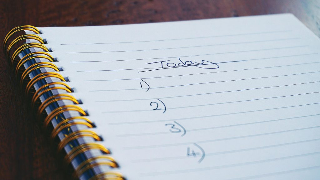 A close-up of an open spiral notebook with the word "today" written at the top and a list started below, symbolizing daily planning and goal setting.
