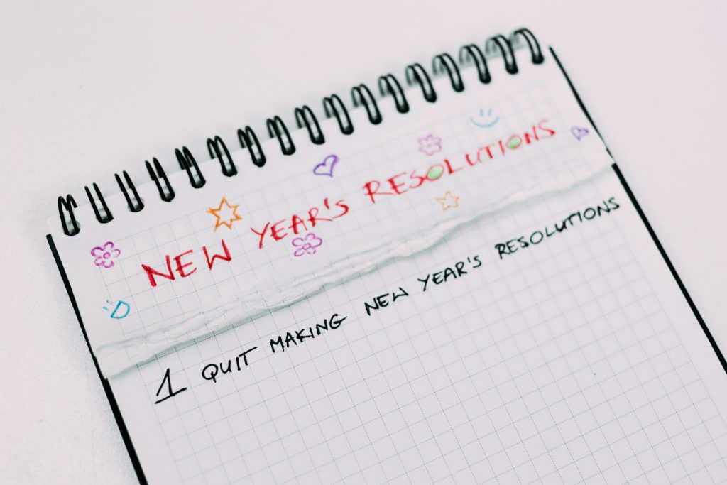 A close-up of a notebook page labeled "new year's resolutions" with colorful doodles and the humorous entry "1. Quit making new year's resolutions" written on it.