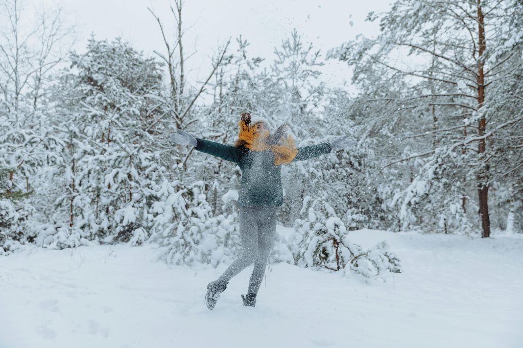 Person joyfully throwing snow in the air in a snow-covered forest, embodying the theme of winter blues.