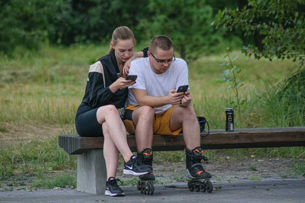 Two people sitting close on a bench, engrossed in their smartphones, illustrating a disconnect in communication which can be challenging for someone with ptsd.