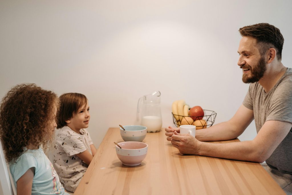 A father sharing a joyful breakfast with his two children at a wooden table, showcasing a nurturing and attentive family environment conducive to managing childhood adhd.
