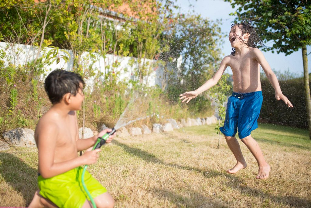 Two boys playing with a water hose in the garden, demonstrating how outdoor play stimulates dopamine production, beneficial for managing adhd.