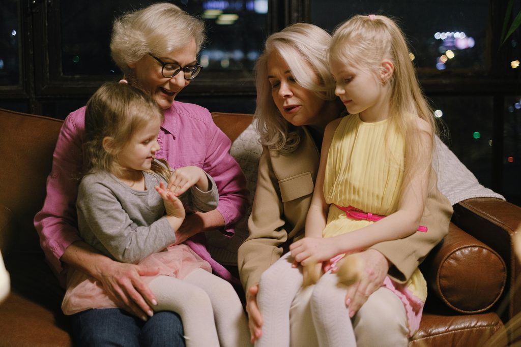 A grandmother, mother, and two young girls sitting closely on a couch, sharing a tender family moment, symbolizing generational healing and bonding.