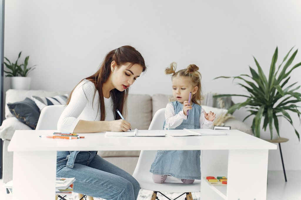 A young mother and her daughter, potentially neurodivergent, engage in a focused drawing session at home.