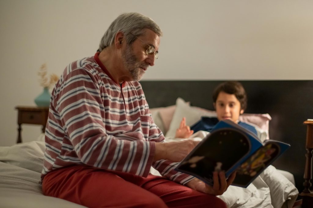 A grandfather reading a bedtime story to his grandson, a nurturing moment that strengthens their bond and contributes to a positive relational experience.