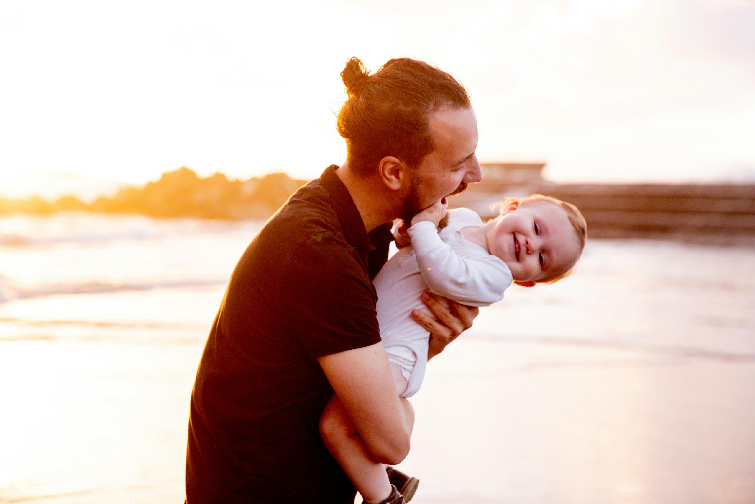 A joyful father holding his smiling baby at the beach, symbolizing recovery from stress and burnout through balance and renewal.