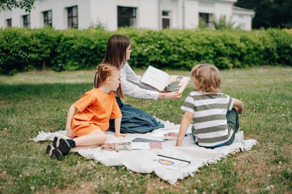 A caregiver reads to two children outdoors, a serene setting that contrasts the intense challenges like postpartum psychosis