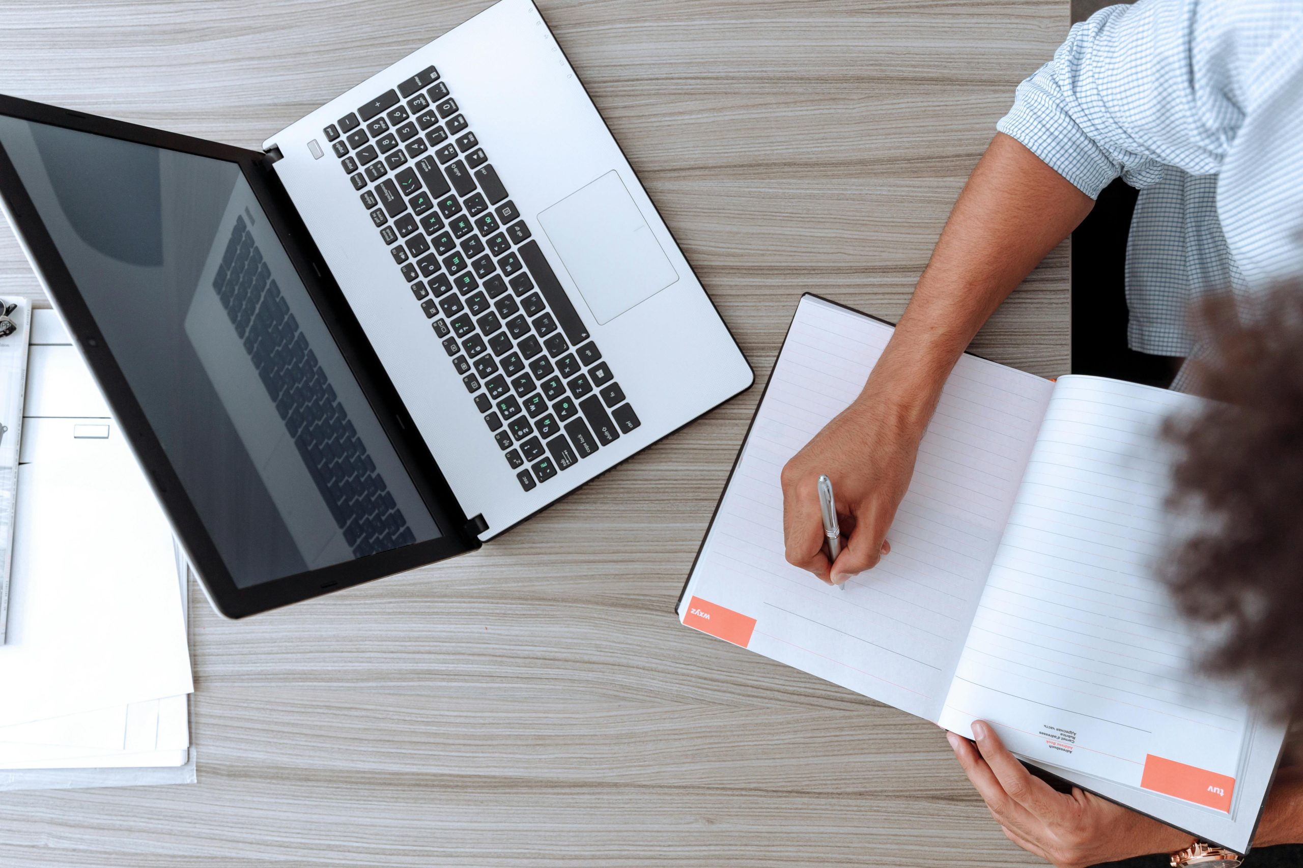 Bipoc-Therapy-Online-Support-Mindshift Overhead view of a bipoc individual writing in a notebook next to a laptop