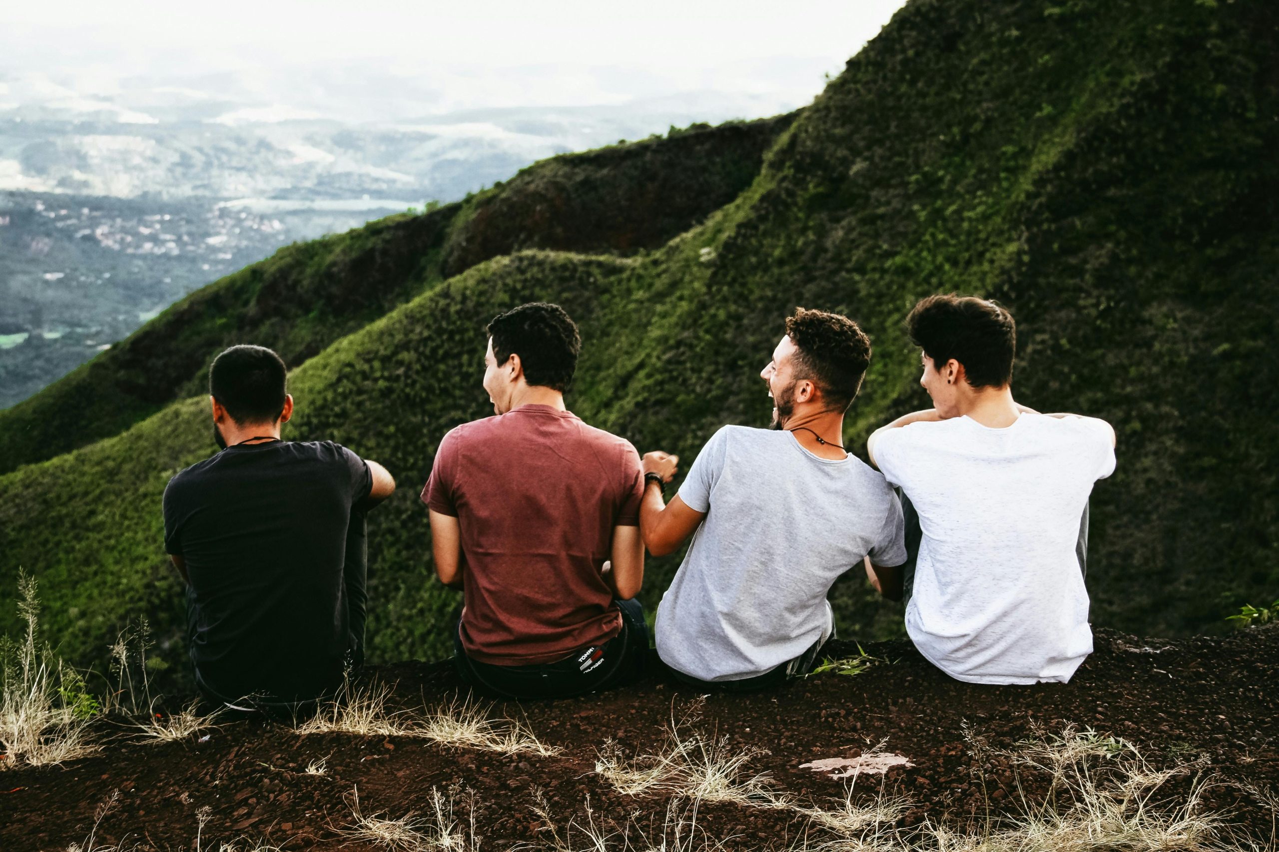 Mens-Therapy-Brotherhood-Connection Four men sitting on a mountain ridge, laughing and bonding with each other
