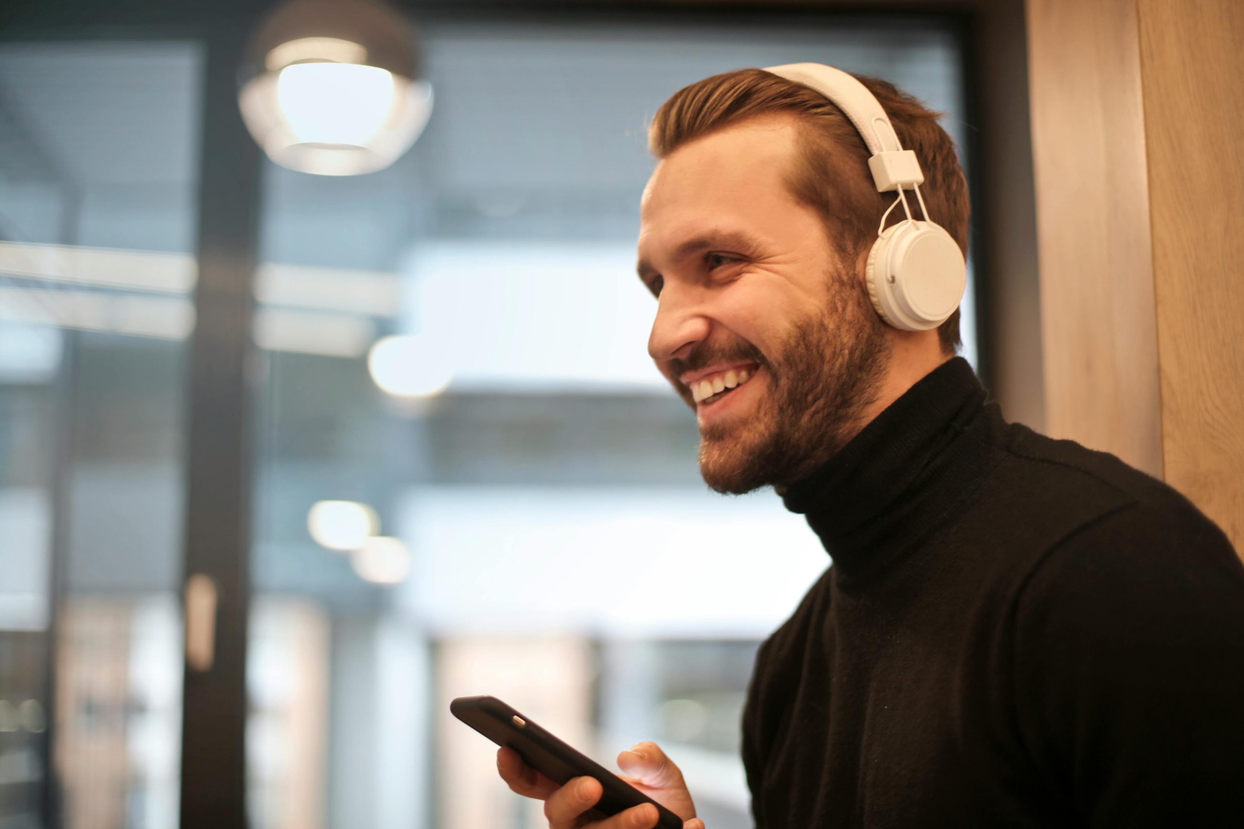 Mens-Therapy-Mental-Health-Relief A man wearing headphones, smiling while holding a phone, looking relaxed and at ease