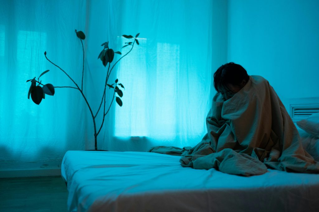 Signs of high functioning depression shown by a person wrapped in a blanket sitting on a bed in a dimly lit room