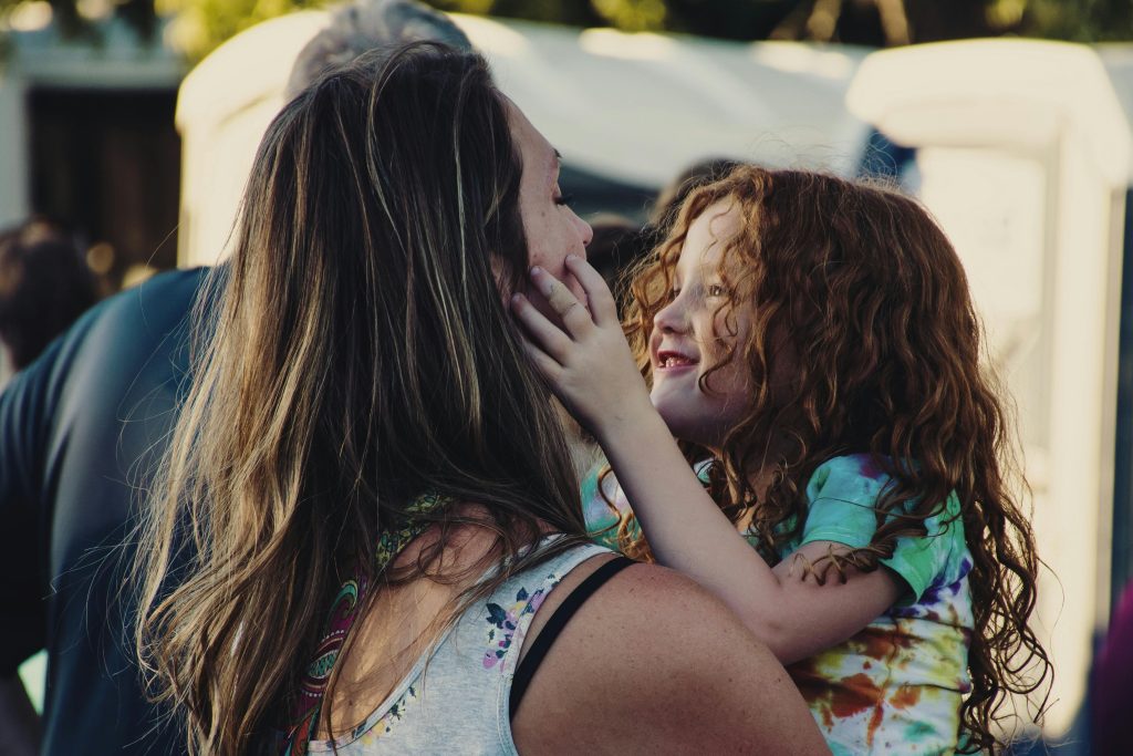 Mom burnout shown through a tired mother being embraced by her cheerful daughter