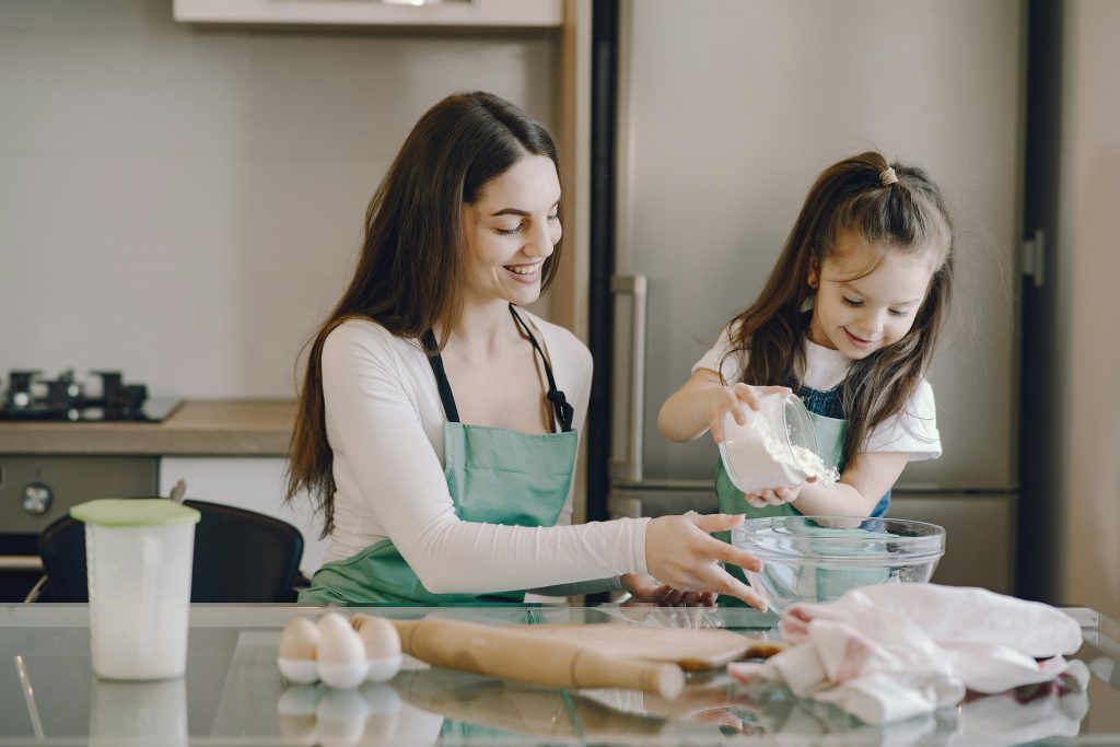 A young girl with autism happily pours flour into a bowl while baking with her mother, illustrating the power of structured routines and shared activities in supporting neurodiverse children.