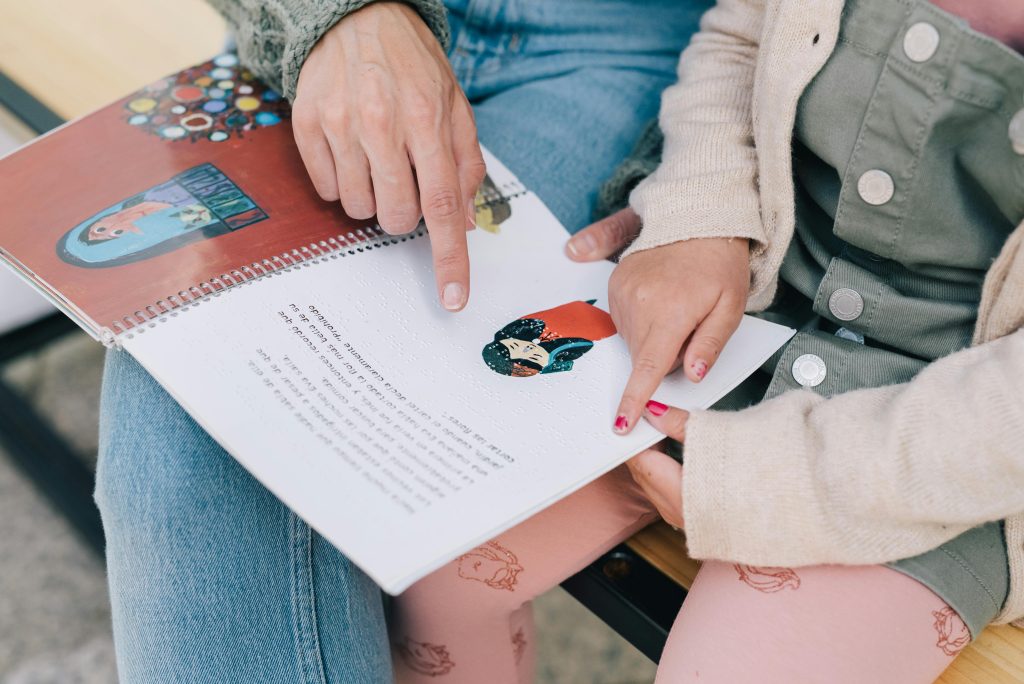 A child and an adult read a tactile braille picture book together, highlighting inclusive learning tools that support children with autism and visual or sensory processing differences.
