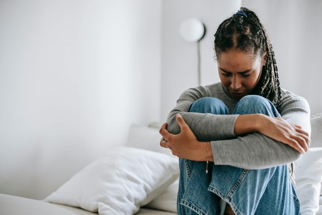 Woman experiencing a panic attack sitting on a bed with her knees to her chest, looking distressed and withdrawn