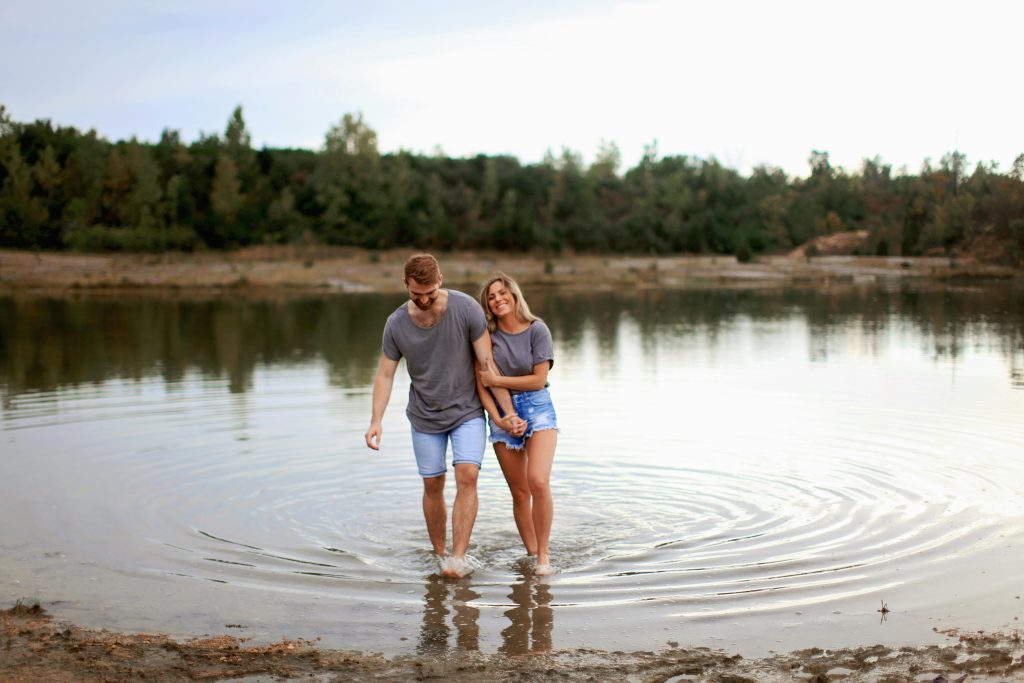 Happy couple holding hands and walking through shallow water, smiling and enjoying each other’s company in nature