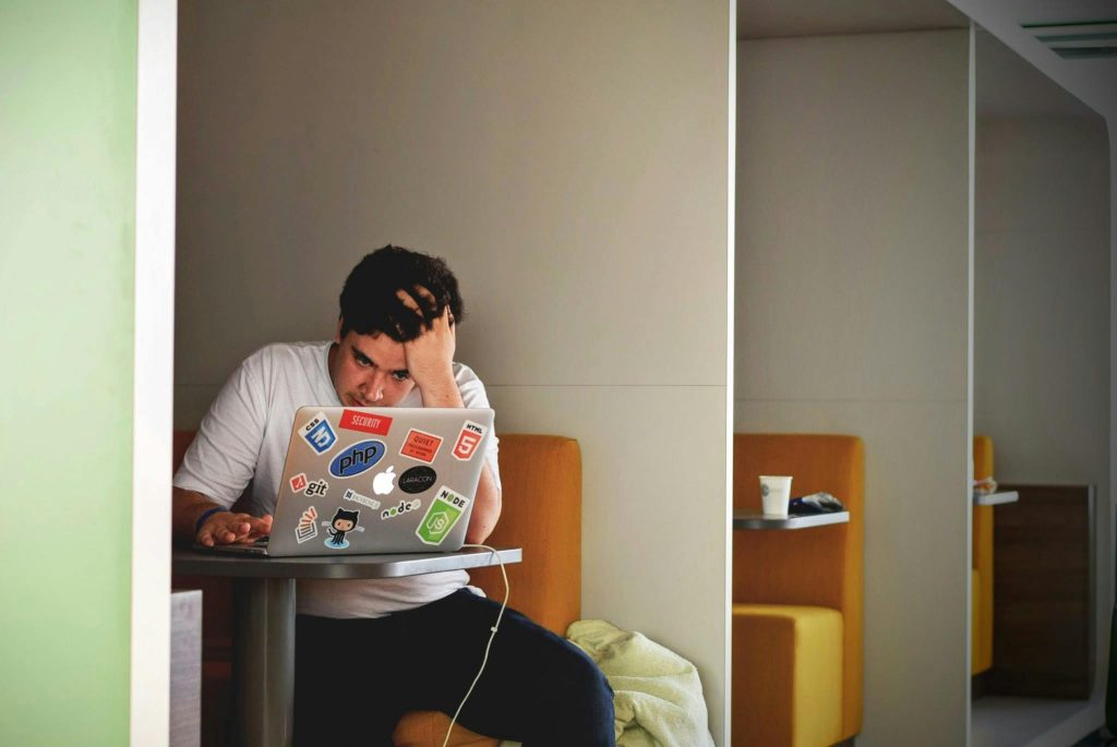 What is anxiety disorder shown by a man looking overwhelmed with his hand on his head while working on a laptop in a booth
