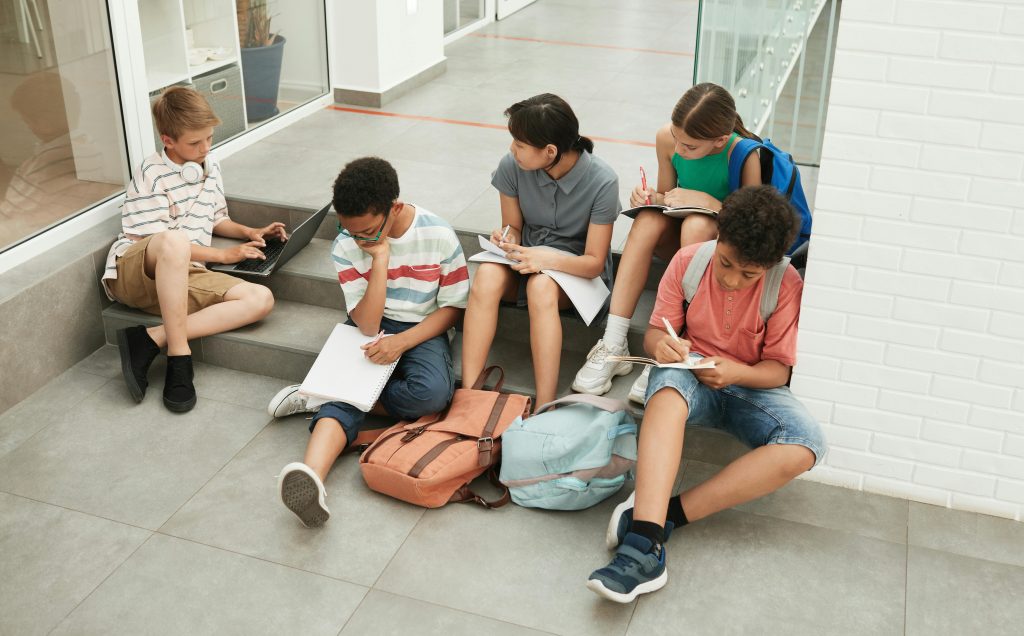 A group of diverse students sitting together, studying with notebooks and a laptop during back-to-school season.