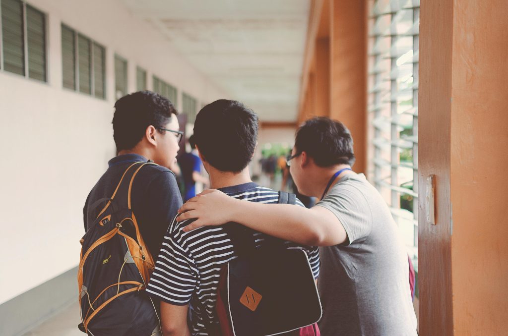 A group of teenage boys walking in a school hallway, one boy has his arm supportively around another, symbolizing back-to-school mental health support and peer connection.