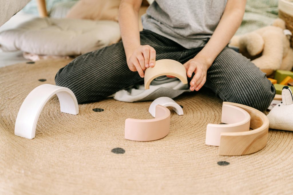 Child playing with curved wooden toys on a rug.