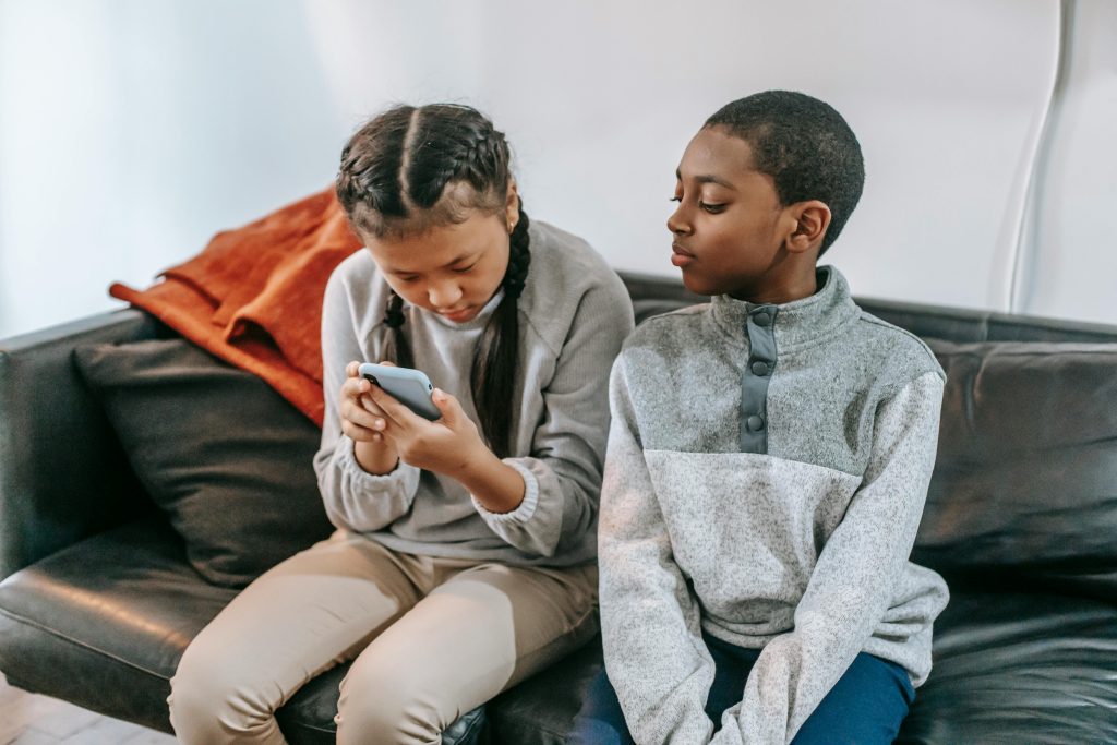 Two kids sitting on a couch, focused on a smartphone together.