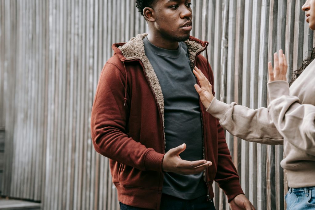 A man in a red hoodie having a tense conversation, with another person holding up their hand as a boundary.