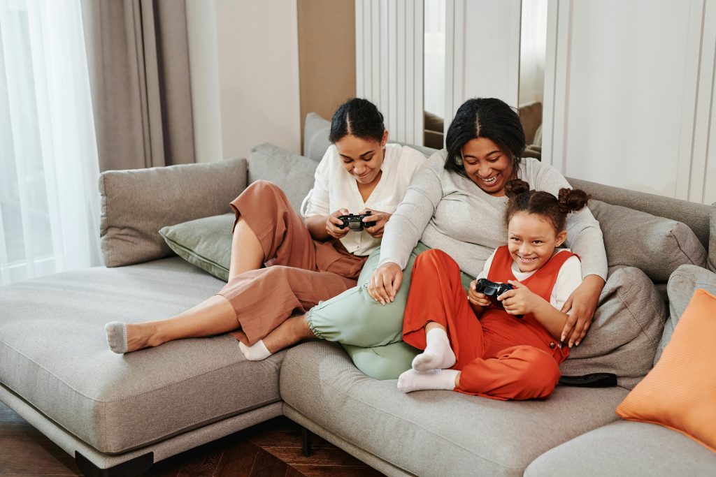 A joyful family playing video games on the couch together, reflecting positive engagement in a trauma-informed parenting environment.