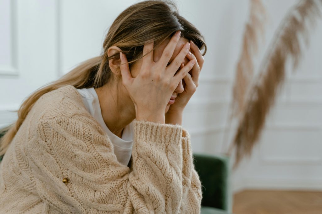 A distressed woman sitting on a green couch with her face buried in her hands, symbolising emotional overwhelm or internalised distress, often used to depict repression or suppression of feelings.