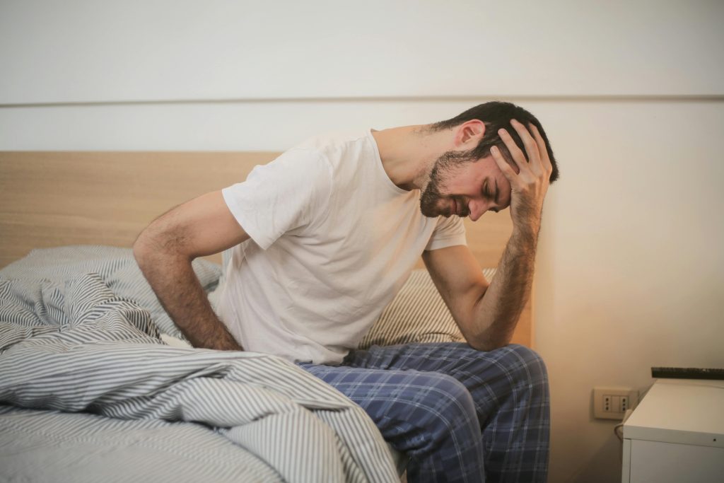 Man in bed holding head, showing signs of stress (lower cortisol)