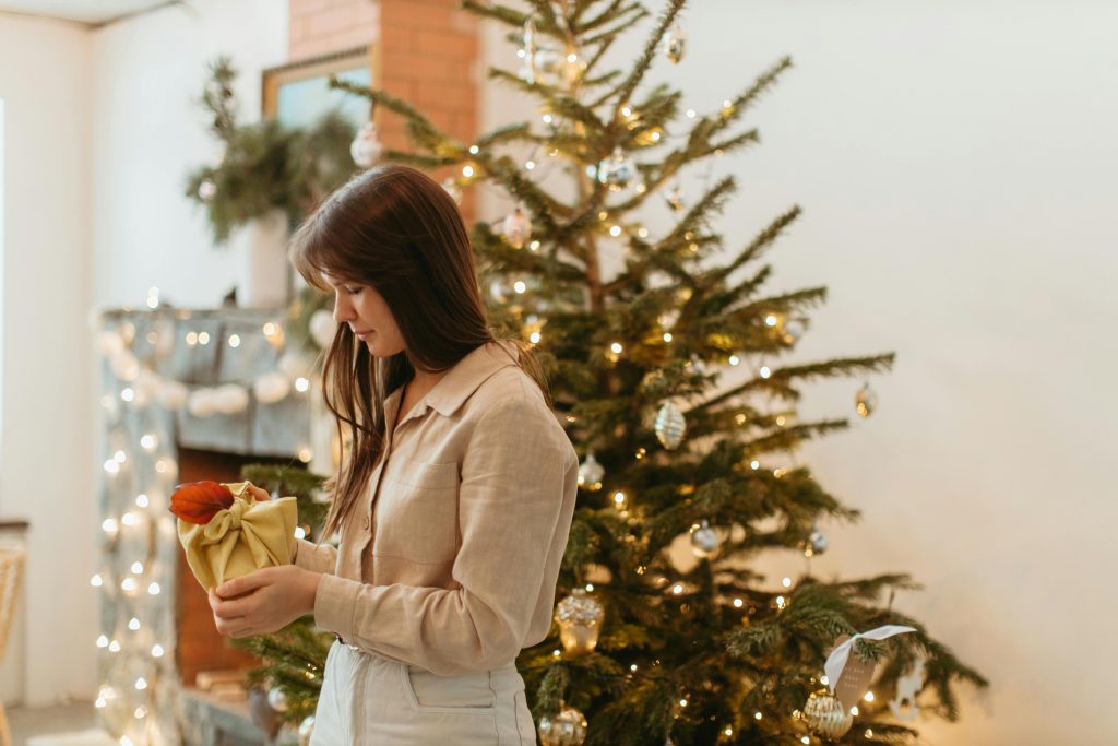 Woman standing alone with a wrapped gift symbolizing introvert holiday tips for quiet moments.