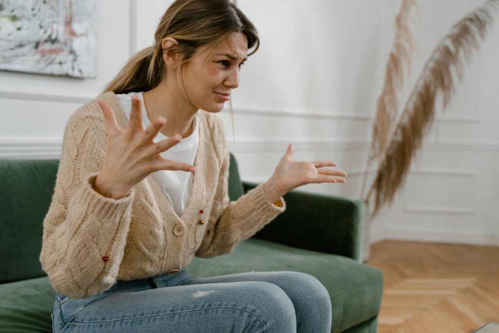 Woman gesturing with frustration while sitting on couch, reflecting how to stop feeling anxious in stressful moments