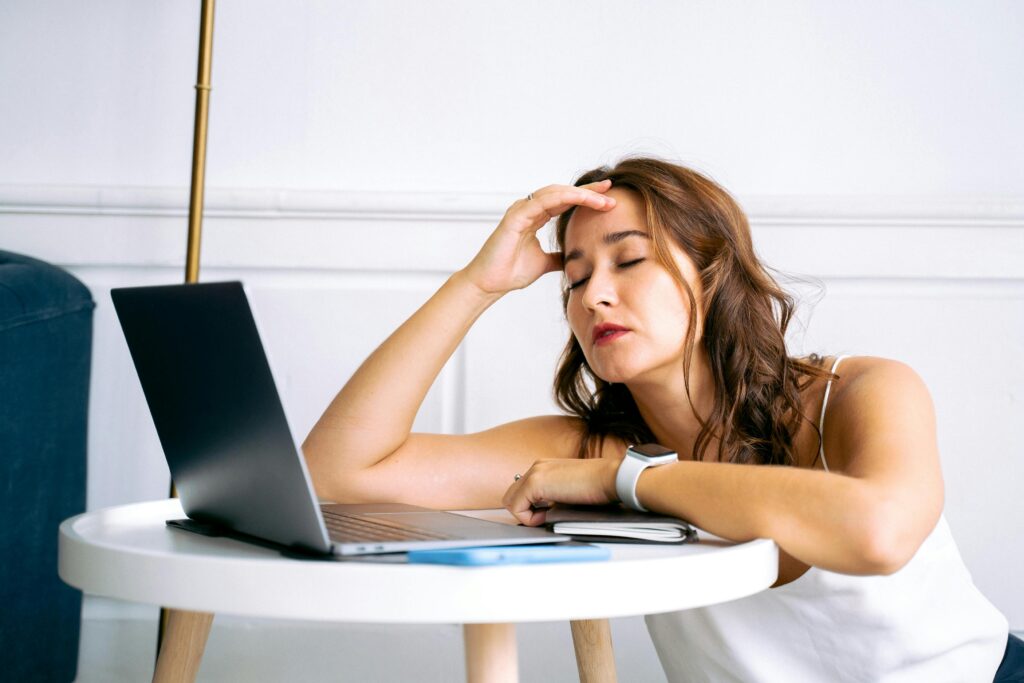 Woman leaning on table with eyes closed beside laptop, showing why am i always so tired working from home