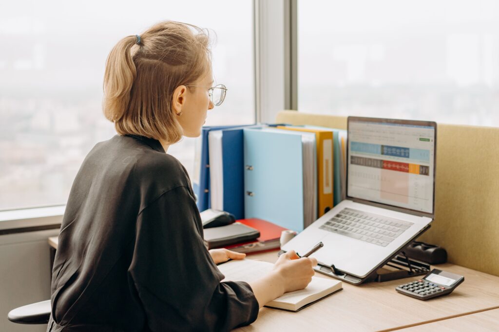 Woman reviewing work on laptop and taking notes, illustrating perfectionism in women in a professional setting
